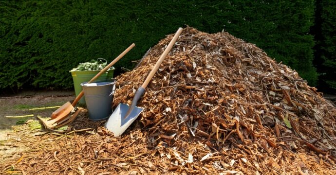 n gros tas de broyat avec une pelle et quelques seau posés au sol. En arrière plan, des bra